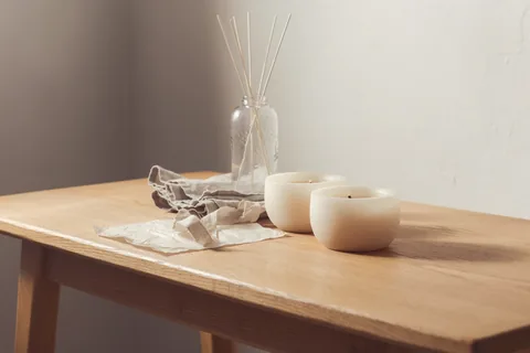 Two candles and a bottle of reed stems on a scrubbed oak table.
