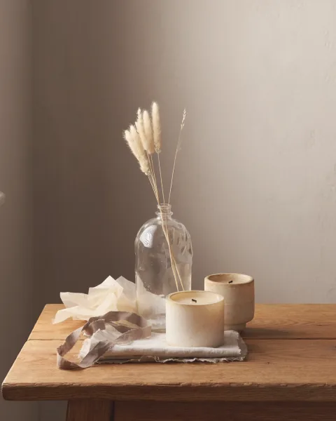 Two candles and a bottle of reed stems on a scrubbed oak table.