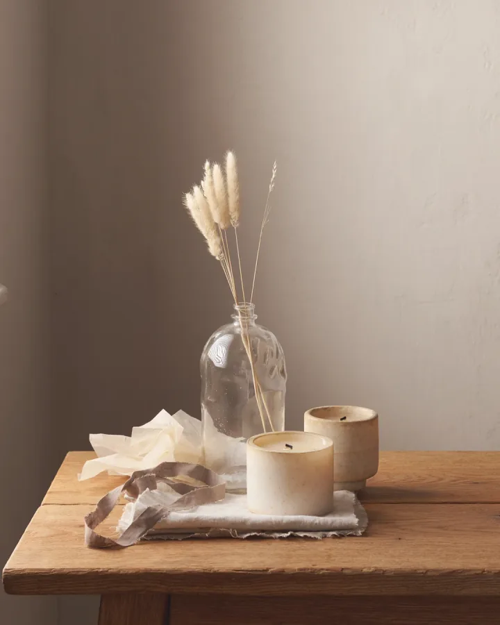 Two candles and a bottle of reed stems on a scrubbed oak table.