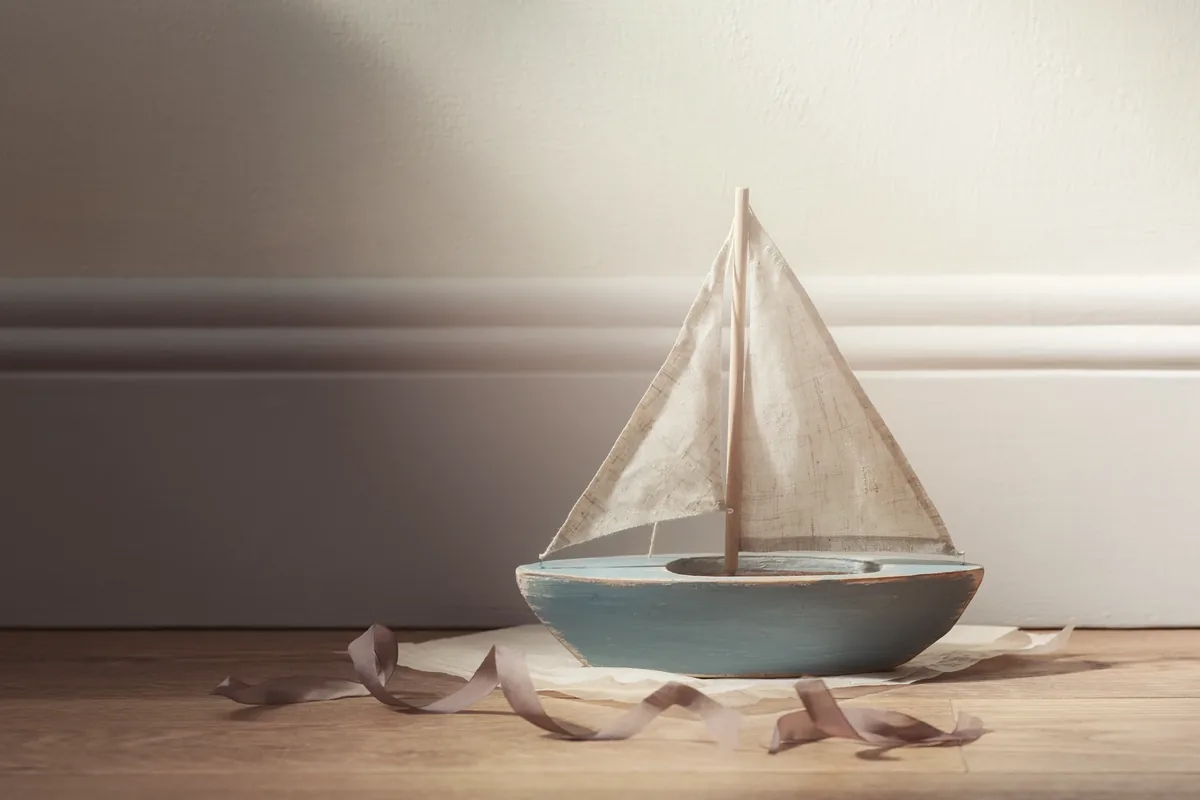 A painted wooden toy sailing boat on tissue on a bare wooden floor.