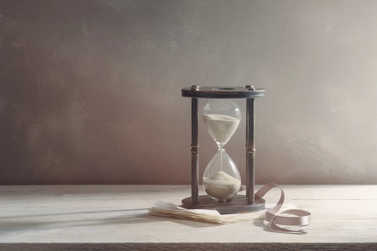 A glass and blackened-steel sand timer on folded tissue with a loose ribbon.