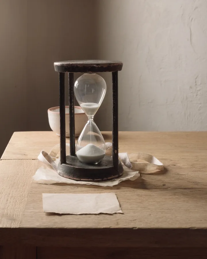 A glass and blackened-steel sand timer on folded tissue with a loose ribbon.