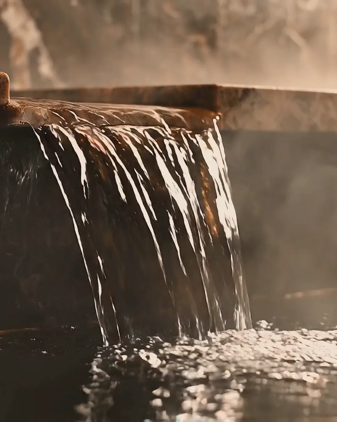 Water sliding over a marble edge into a dark pool, steam rising behind it.