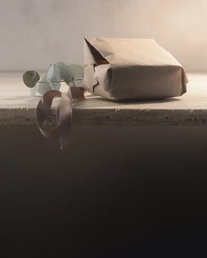 A paper-wrapped parcel with a loose ribbon and a eucalyptus sprig on a stone shelf.