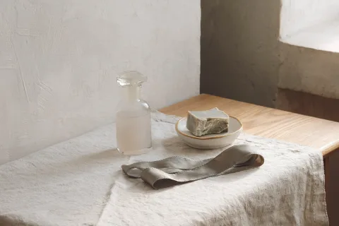A bar of soap on a dish and a stoppered bottle on a linen-covered dressing table.