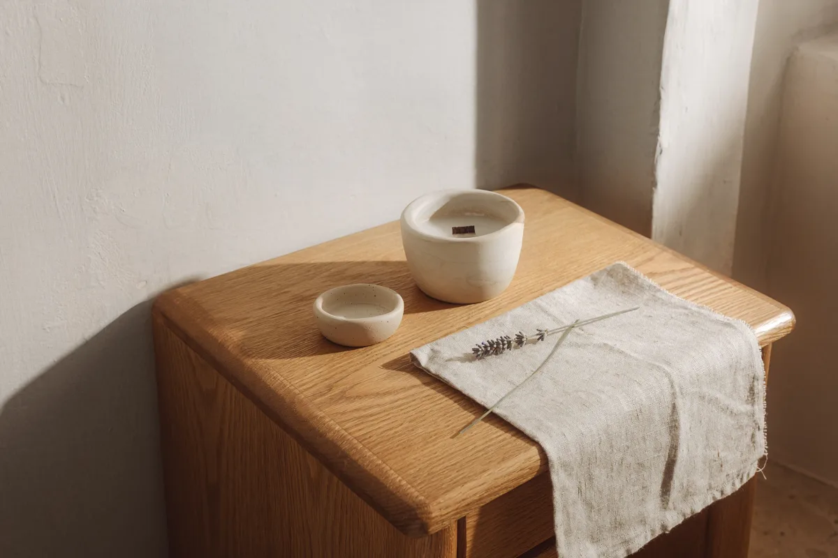 A folded cloth, a candle and a lavender sprig on a bedside table.