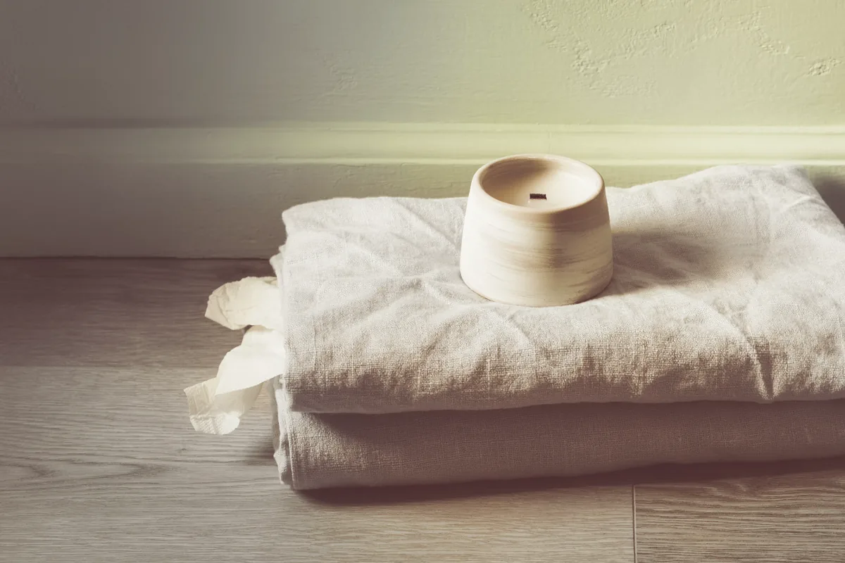 Two folded linen towels and a candle on bare floorboards.