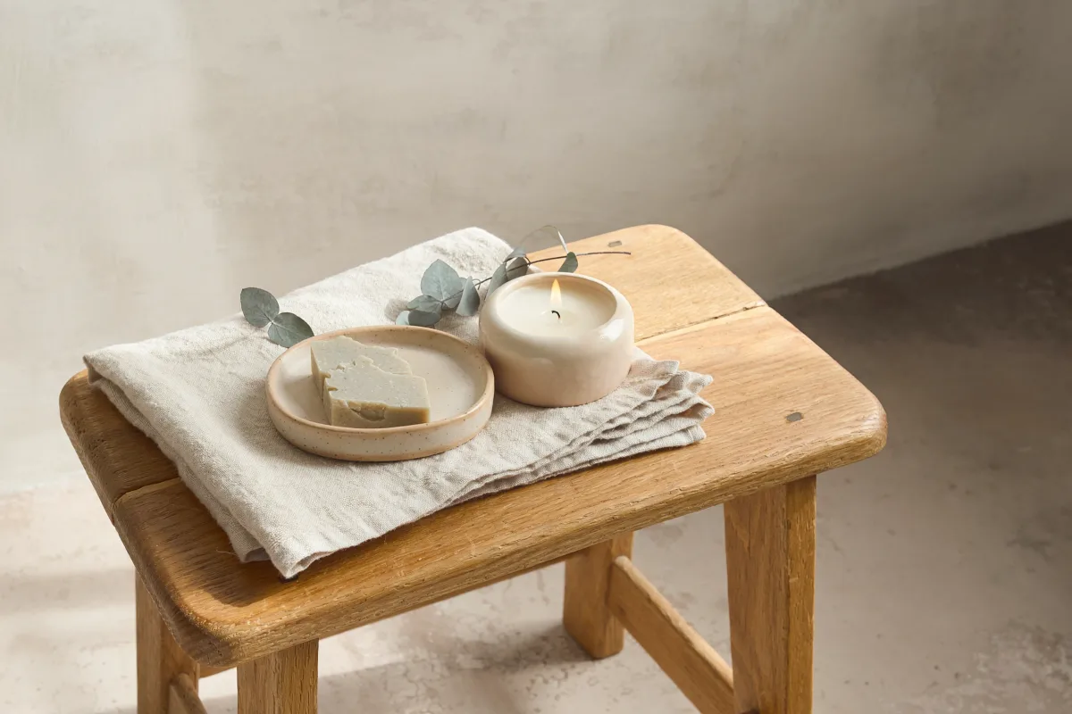 A folded towel, a bar of soap and a lit candle on an oak stool.