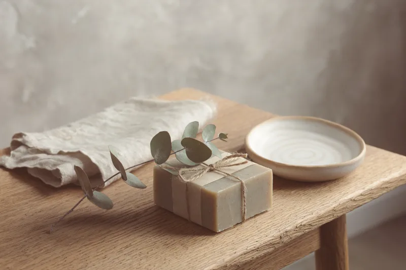 A bar of soap wrapped in paper and tied with string, a eucalyptus sprig across it