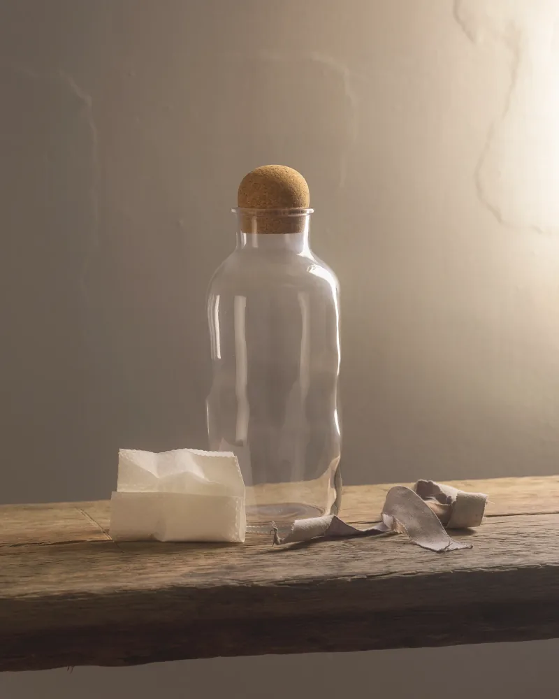 A corked glass bottle and a folded paper wrap on a worn oak bench.