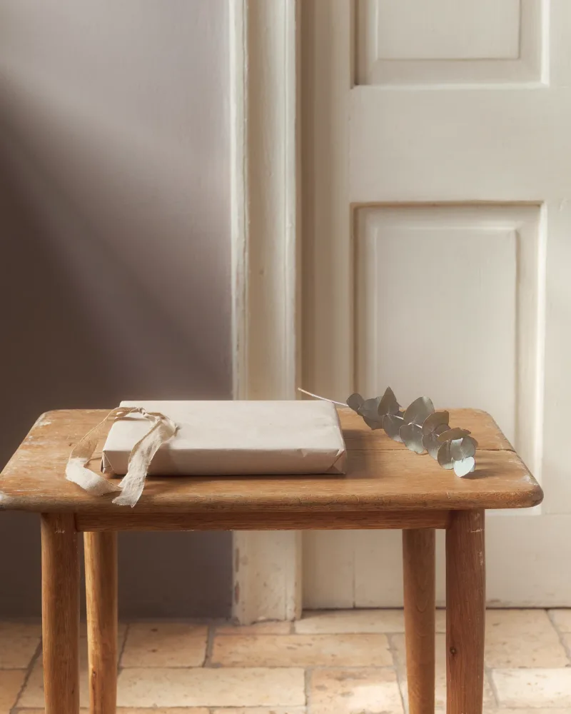 A paper parcel tied with a ribbon on a hall table beside a painted door.